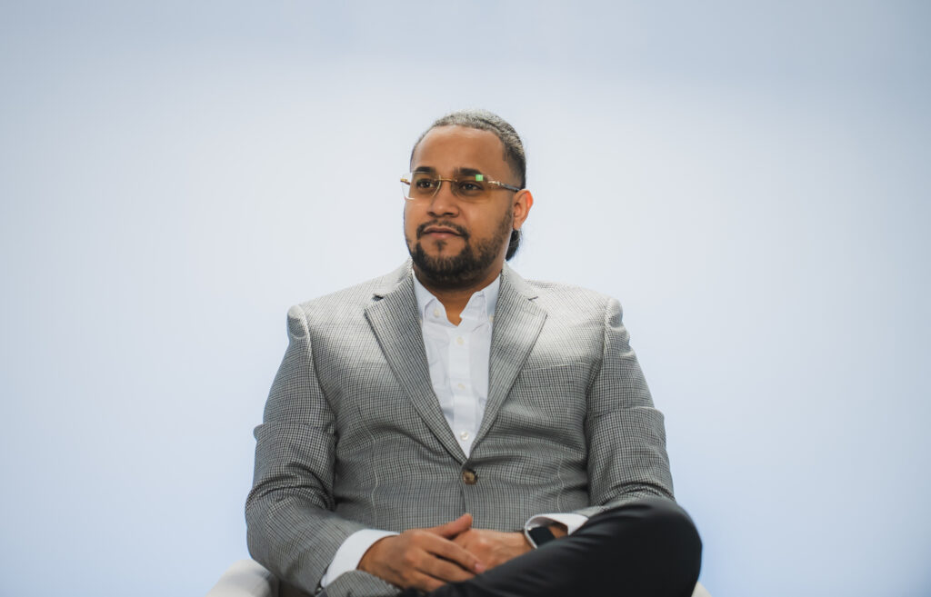 A gentleman in a studio, dressed professionally, standing near cameras and lighting equipment with a focused expression.