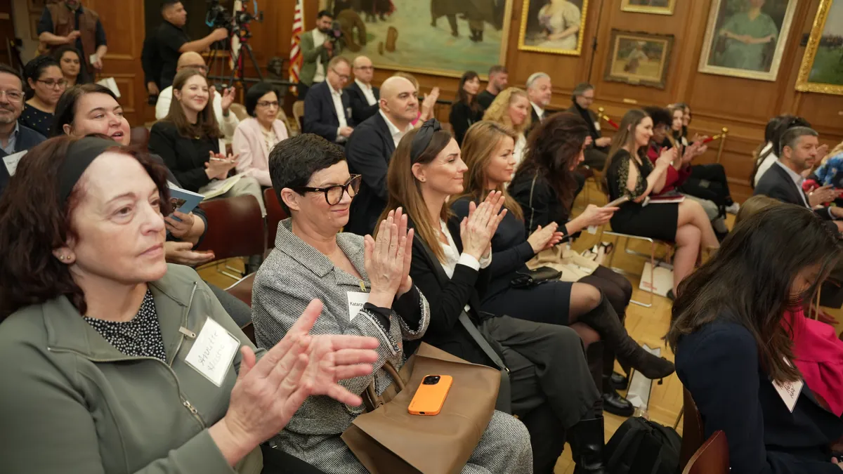 Audience members applauding at an event in a wood-paneled hall