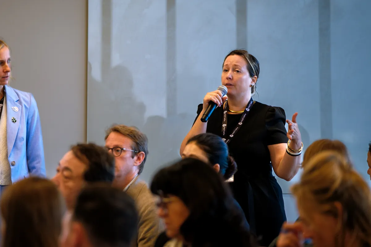 Woman asking a question with a microphone while seated attendees look on at a conference