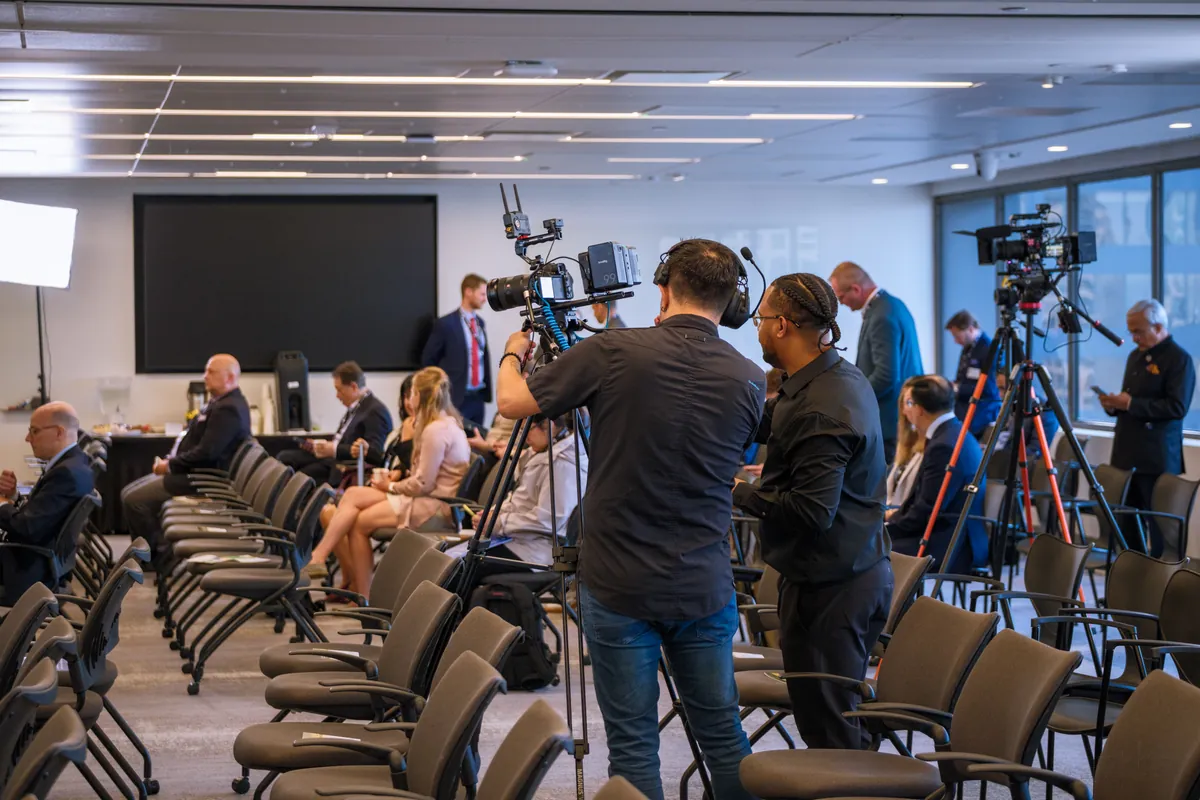 Video crew with cameras on tripods in a conference room with rows of chairs