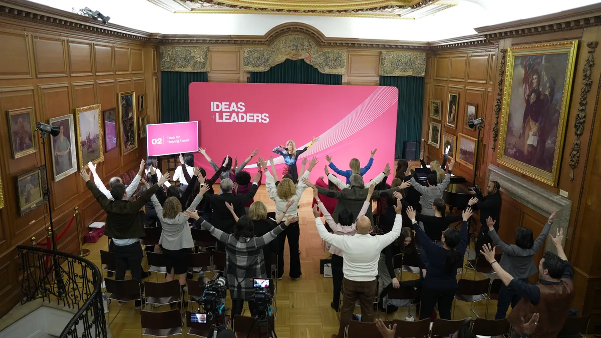 Audience with raised arms facing a pink stage backdrop in a wood-paneled historic room