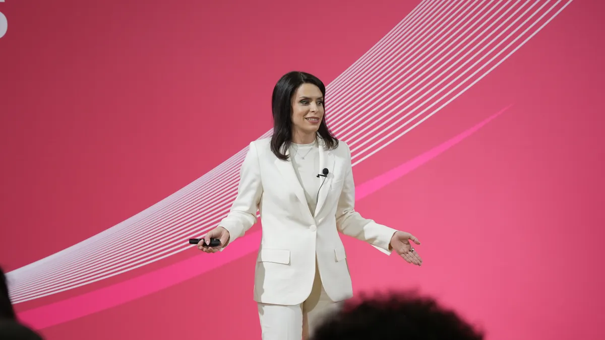 Woman in a white suit presenting on stage against a pink backdrop