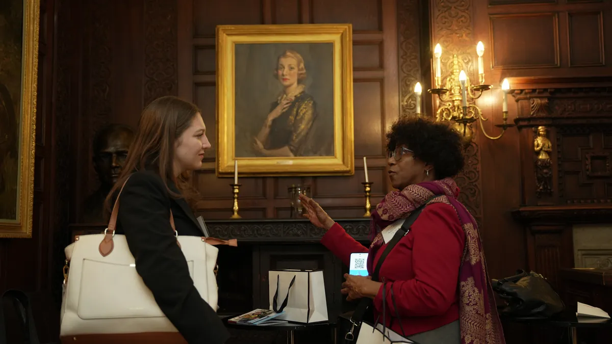 Two people talking at a reception in a room with a framed portrait on the wall