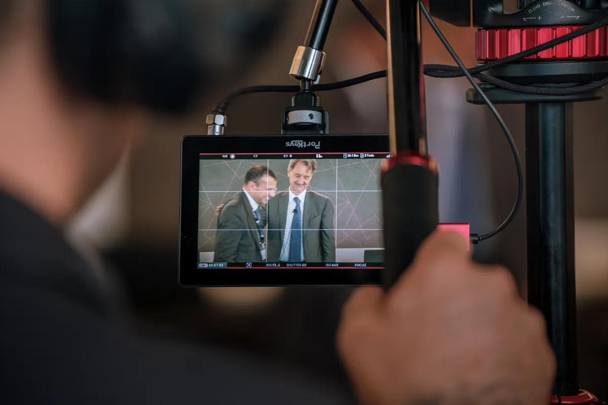 Videographer holding a camera with a monitor showing a recorded panel